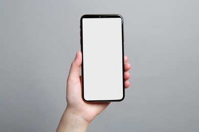 Woman holding smartphone with blank screen on grey background, closeup. Mockup for design