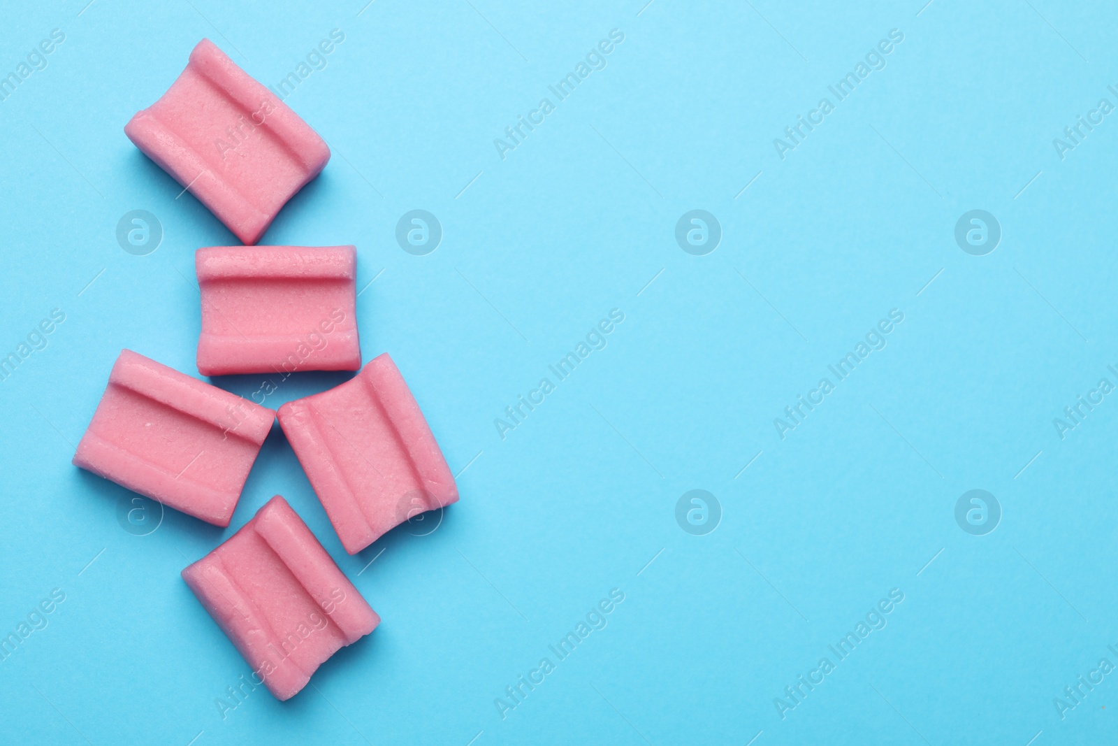 Photo of Tasty pink chewing gums on light blue background, flat lay. Space for text