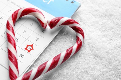 Photo of Saint Nicholas Day. Heart shape frame of candy canes and calendar with marked date December 19 on snow, closeup