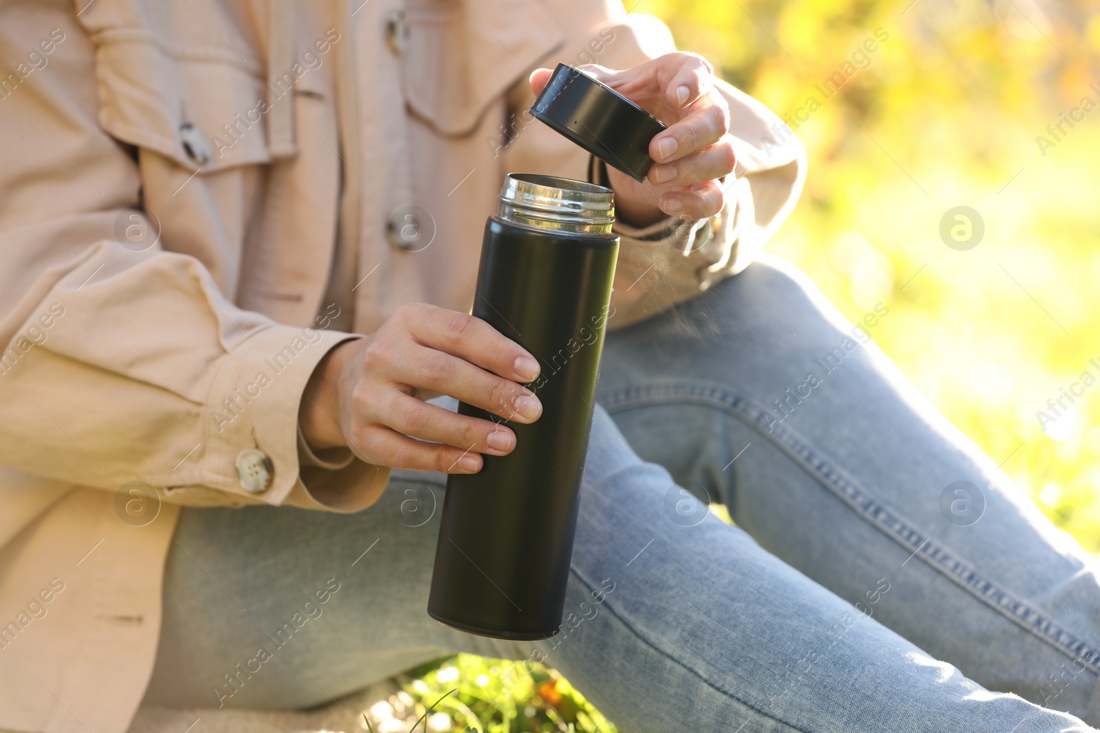 Photo of Woman opening thermos outdoors on sunny day, closeup