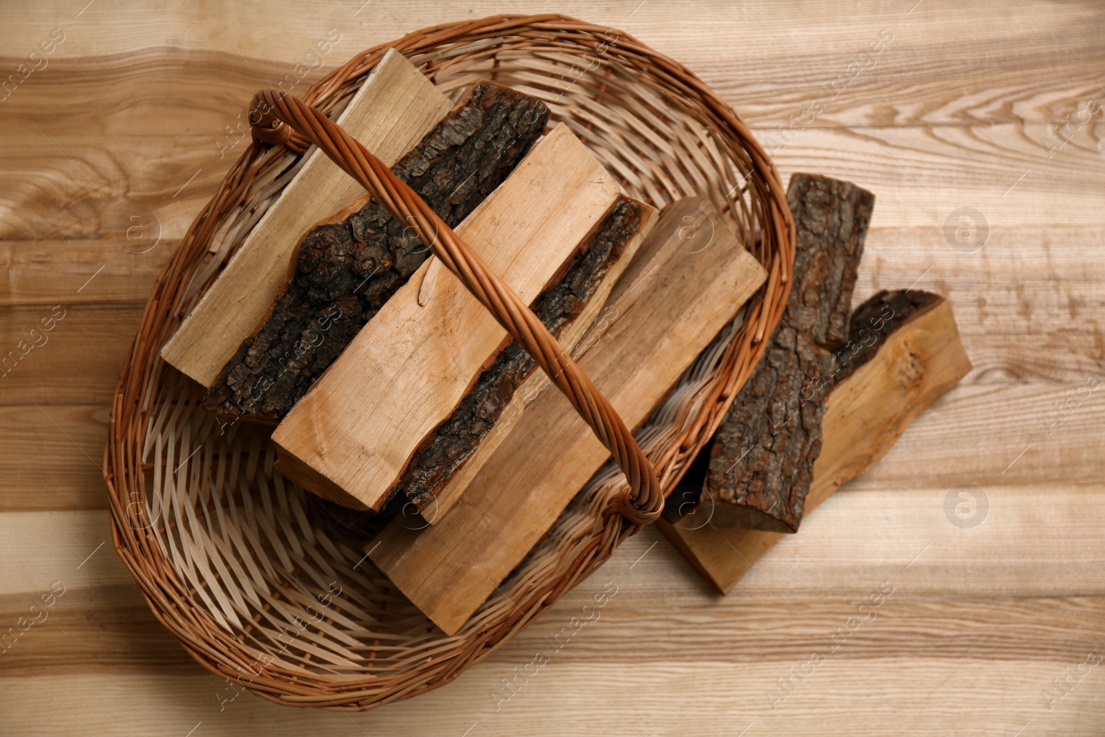 Photo of Wicker basket and firewood on floor indoors, flat lay