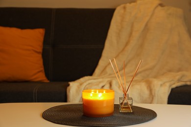 Photo of Beautiful candle and reed air freshener on white table indoors. Cosy atmosphere