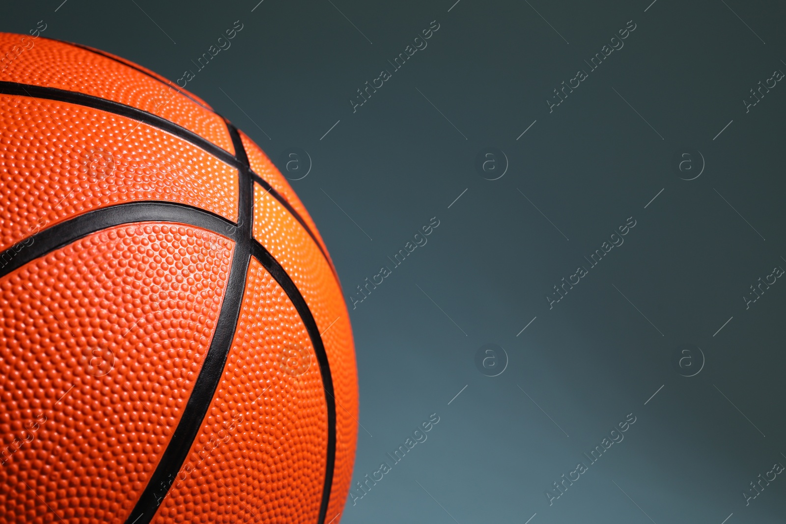 Photo of One orange basketball ball on dark grey background, closeup. Space for text