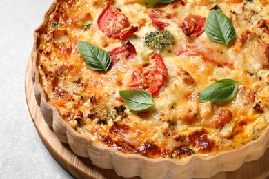 Tasty quiche with cheese, tomatoes and basil leaves on light grey table, closeup