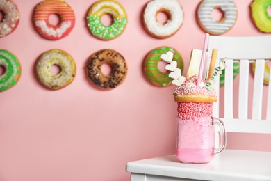 Photo of Tasty milk shake with sweets in mason jar on chair indoors. Space for text