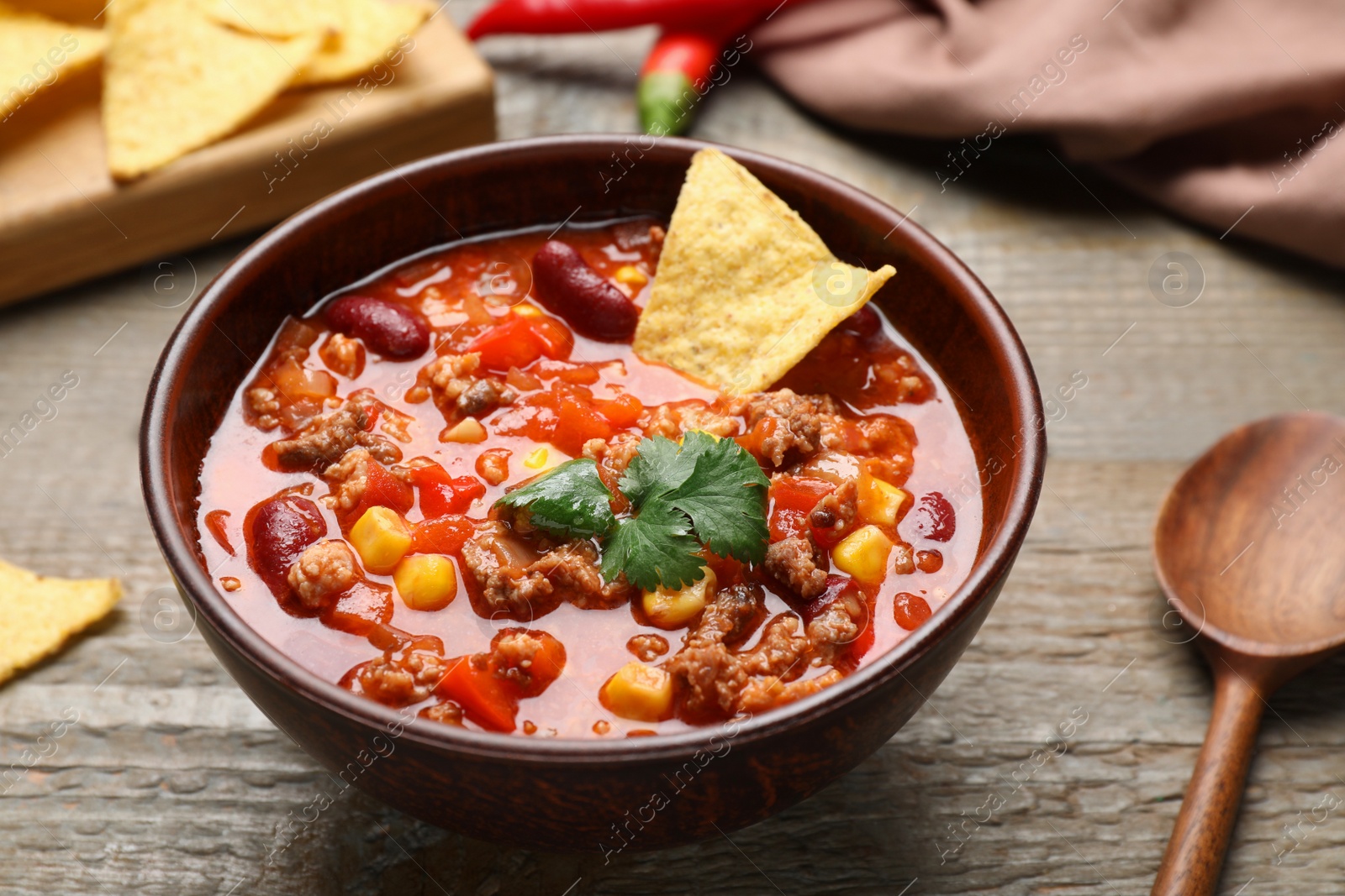 Photo of Bowl of tasty chili con carne with nachos on wooden table, closeup