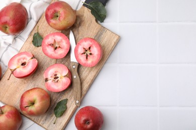 Photo of Tasty apples with red pulp, leaves and knife on white tiled table, flat lay. Space for text