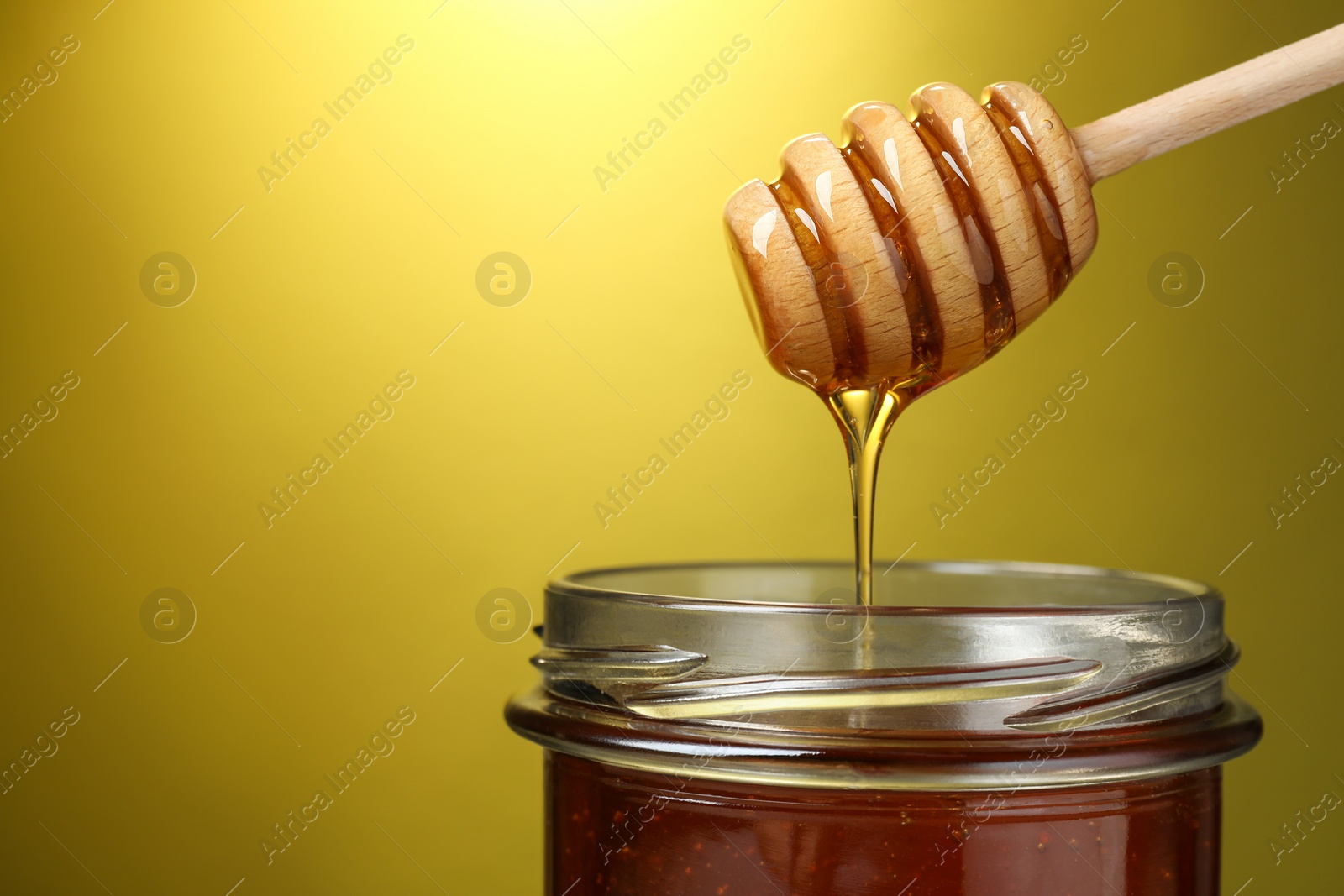 Photo of Pouring tasty honey from dipper into glass jar on golden background, closeup. Space for text