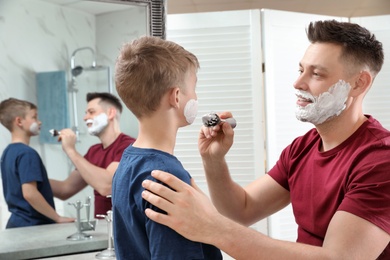 Photo of Dad applying shaving foam on son's face at mirror in bathroom