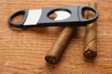 Photo of Cigars and guillotine cutter on wooden table, closeup