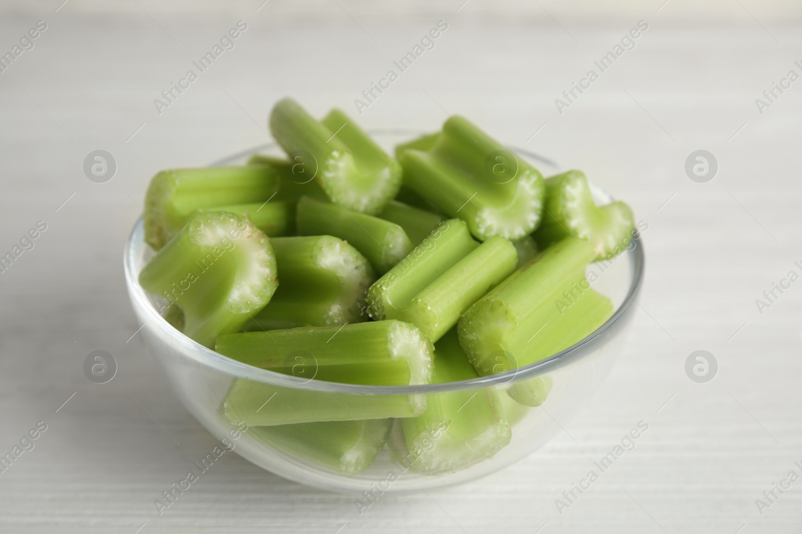 Photo of Cut celery in glass bowl on white wooden table, closeup