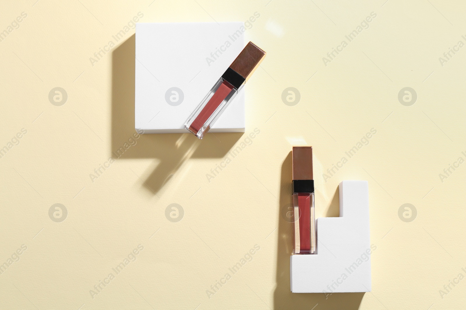 Photo of Lip glosses and podiums on pale yellow background, top view