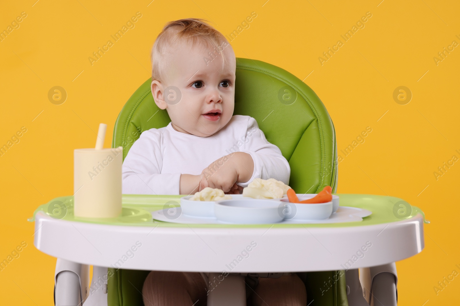 Photo of Cute little baby with healthy food in high chair on orange background