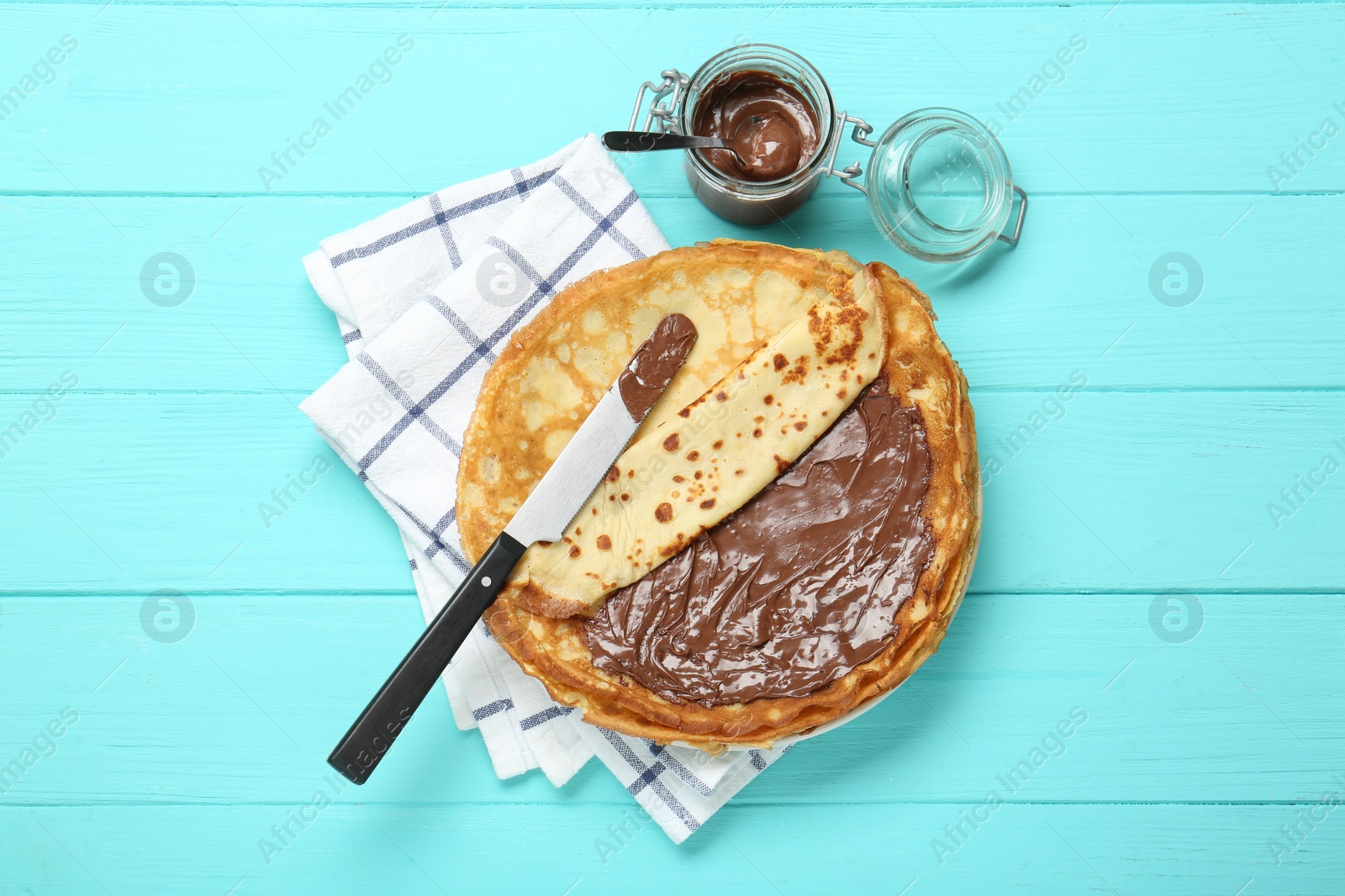 Photo of Tasty crepes with chocolate paste served on turquoise wooden table, flat lay