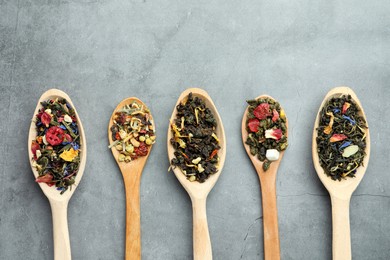 Photo of Different kindsdry herbal tea in wooden spoons on light grey table, flat lay