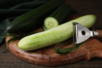 Fresh cucumbers and peeler on wooden table, closeup