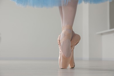 Photo of Ballerina in pointe shoes and light blue skirt dancing indoors, closeup. Space for text