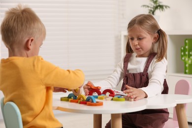 Photo of Little children playing with colorful wooden pieces at white table indoors. Developmental toy