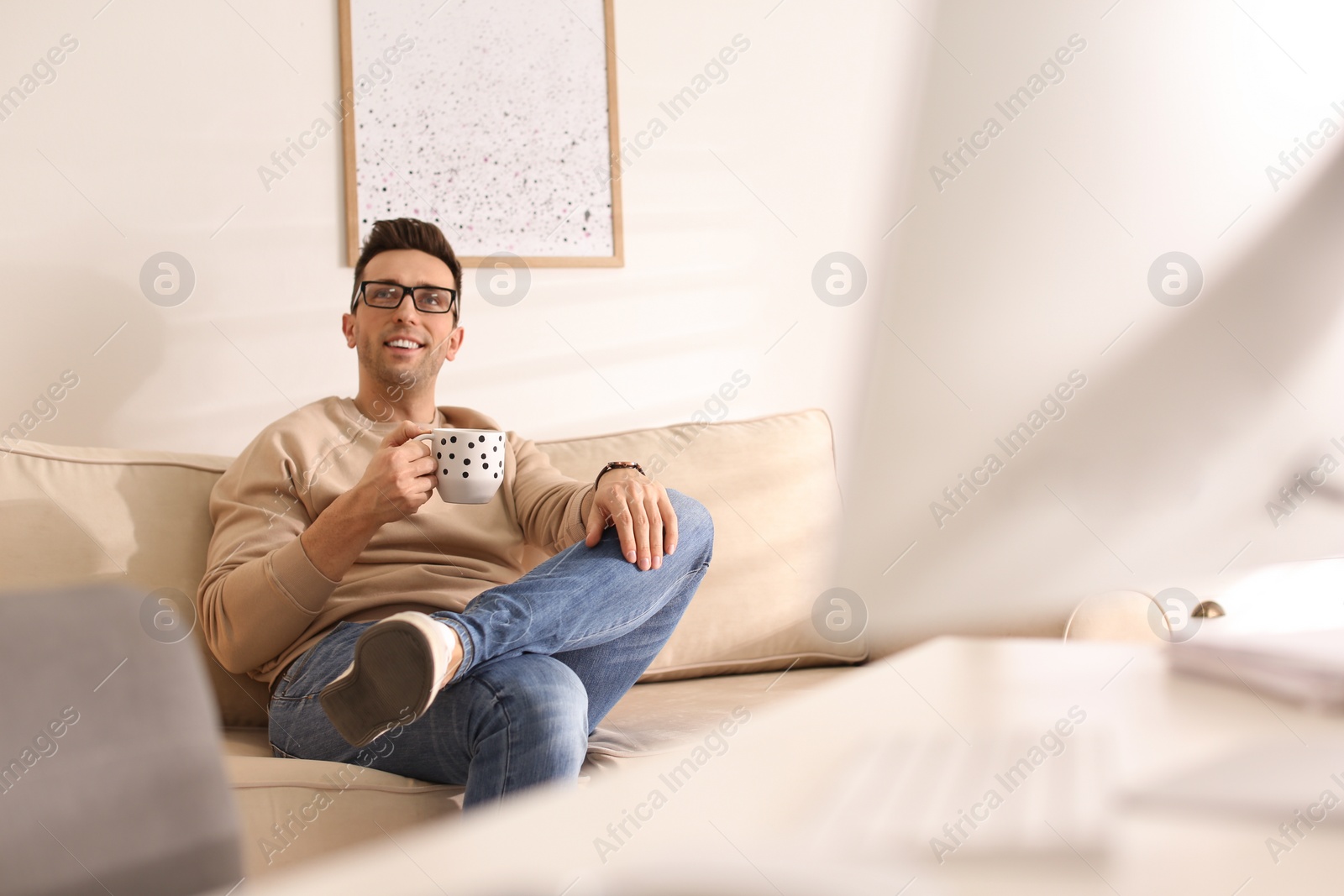 Photo of Young man with cup of drink relaxing on couch in office during break