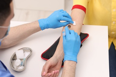 Photo of Doctor taking blood sample from patient with syringe at white table in hospital, closeup