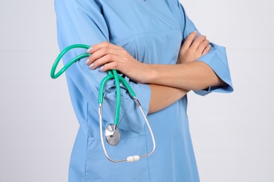 Medical assistant with stethoscope on light background, closeup