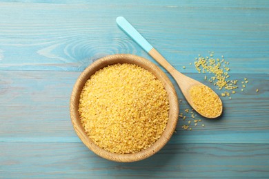 Photo of Bowl and spoon with raw bulgur on light blue wooden table, top view