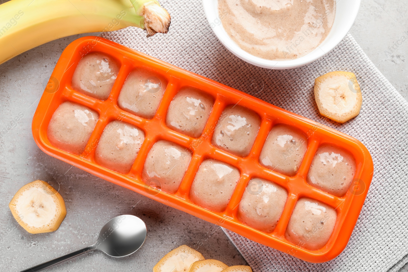 Photo of Banana puree in ice cube tray with fresh banana fruits on grey table, flat lay