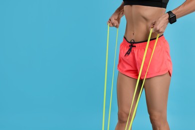 Photo of Woman exercising with elastic resistance band on light blue background, closeup. Space for text