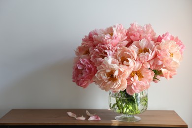 Beautiful pink peonies in vase on table near white wall, space for text