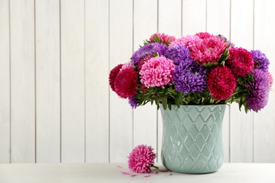 Beautiful asters in vase on table against white wooden background, space for text. Autumn flowers