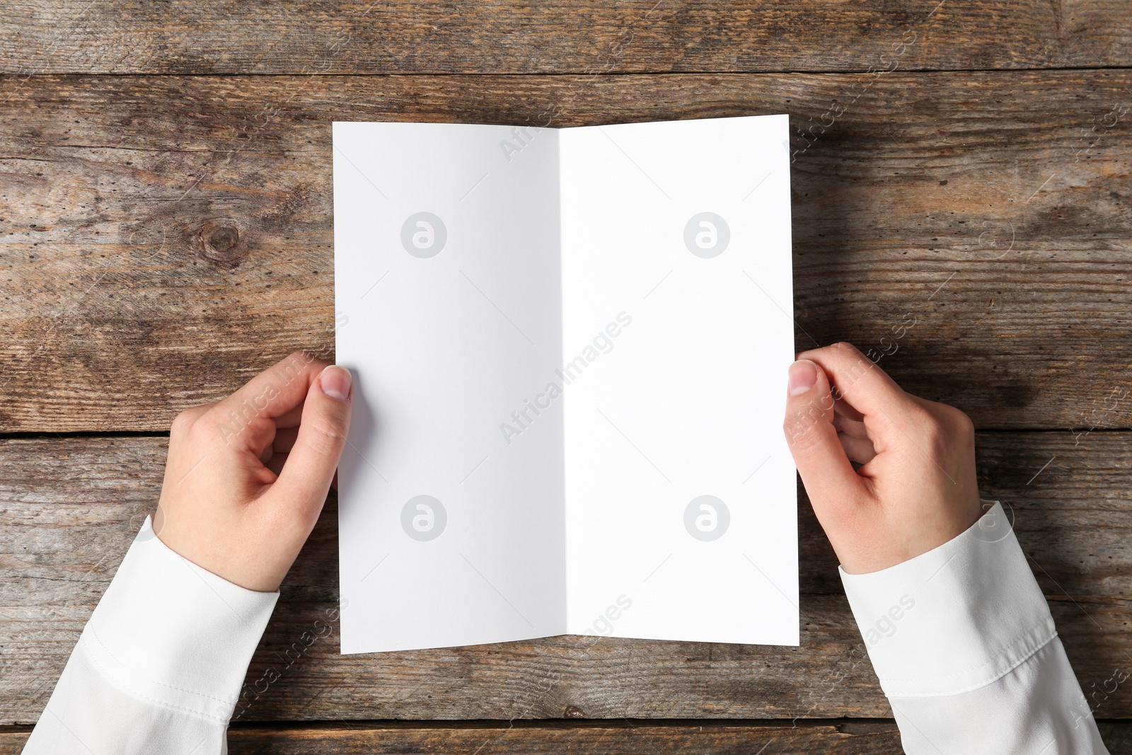 Photo of Woman holding blank brochure mock up on wooden table, top view