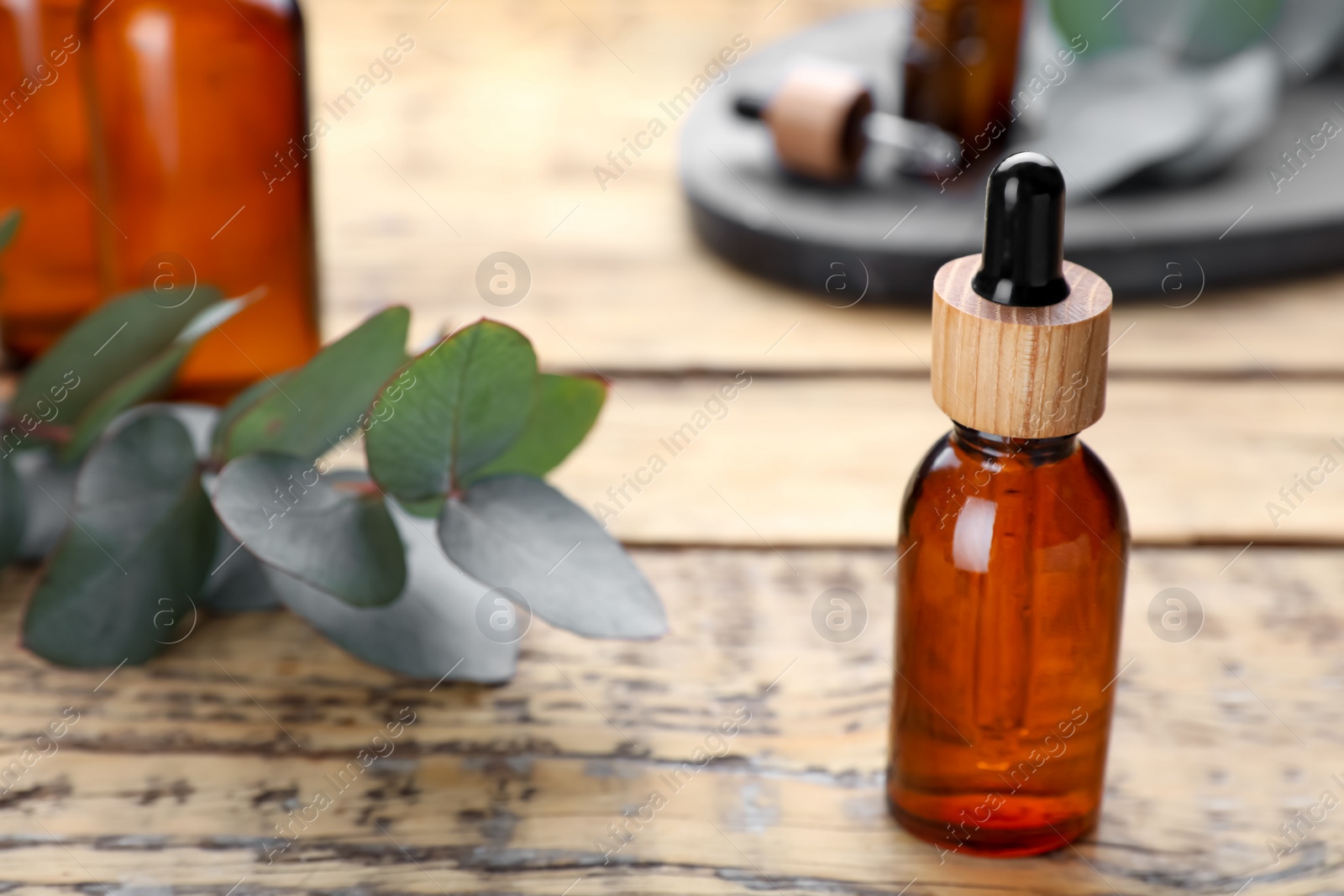 Photo of Bottle of essential oil and eucalyptus branch on wooden table, closeup. Space for text