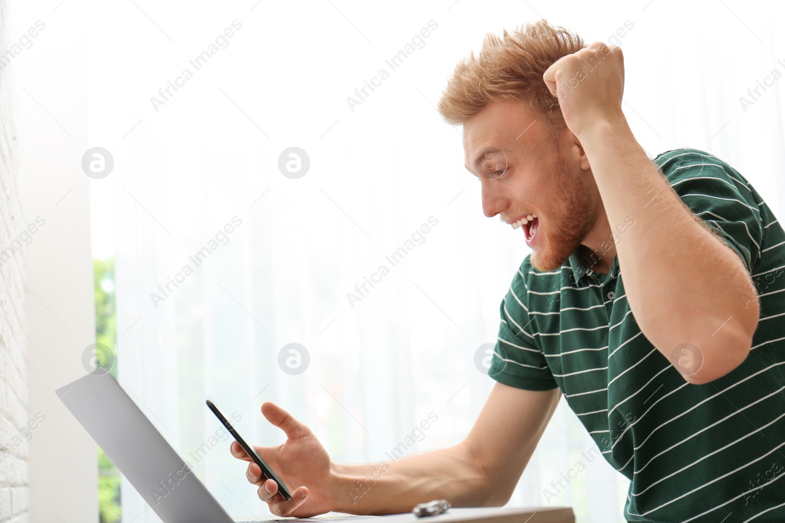 Photo of Happy young man playing online lottery using smartphone indoors