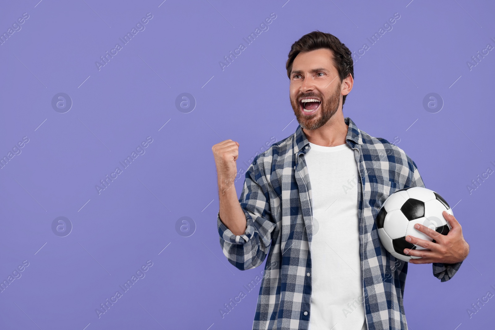 Photo of Emotional sports fan with soccer ball on purple background. Space for text