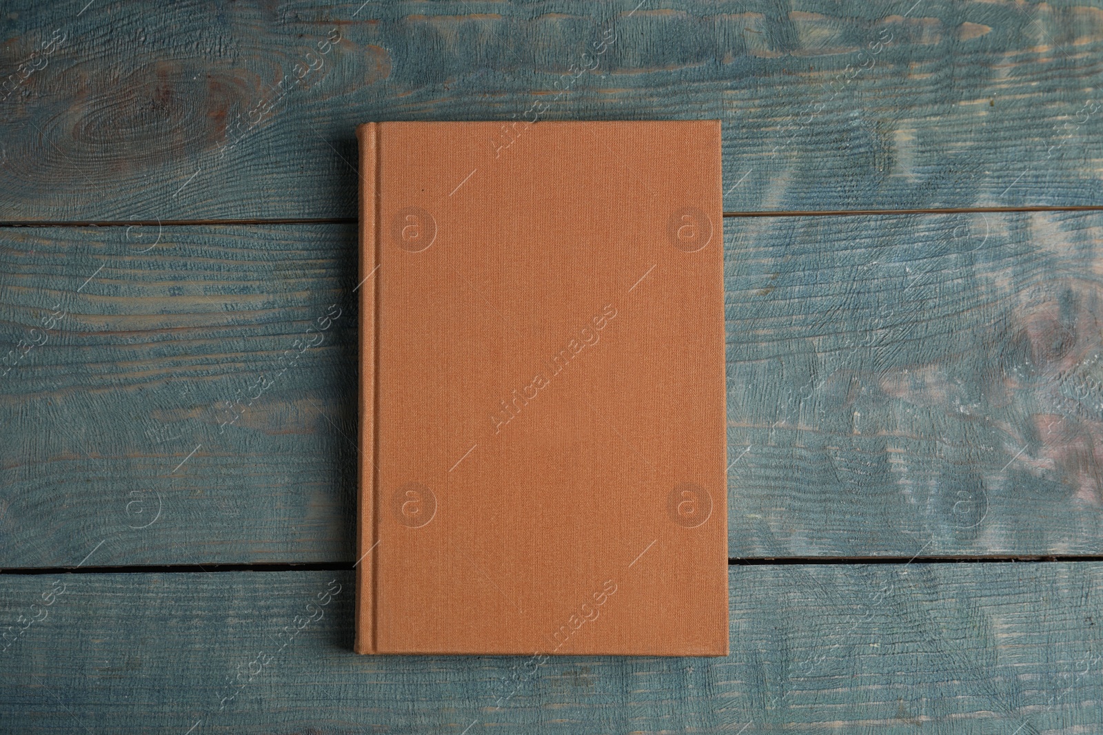 Photo of Hardcover book on light blue wooden table, top view. Space for text