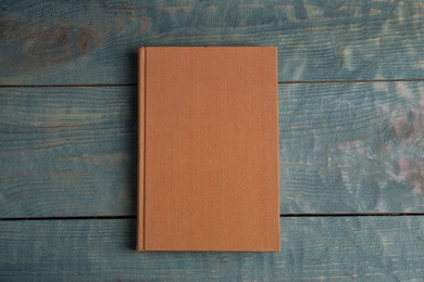 Hardcover book on light blue wooden table, top view. Space for text