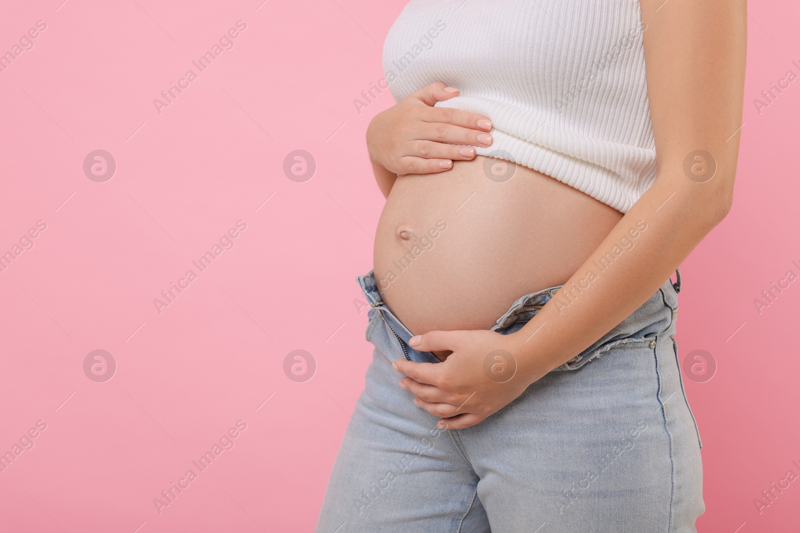 Photo of Pregnant woman in jeans on pink background, closeup. Space for text