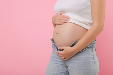 Photo of Pregnant woman in jeans on pink background, closeup. Space for text