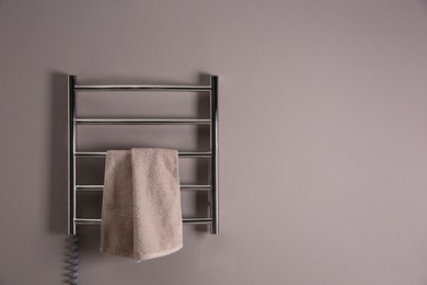 Photo of Modern heated towel rail with warm soft towel on grey wall. Space for text