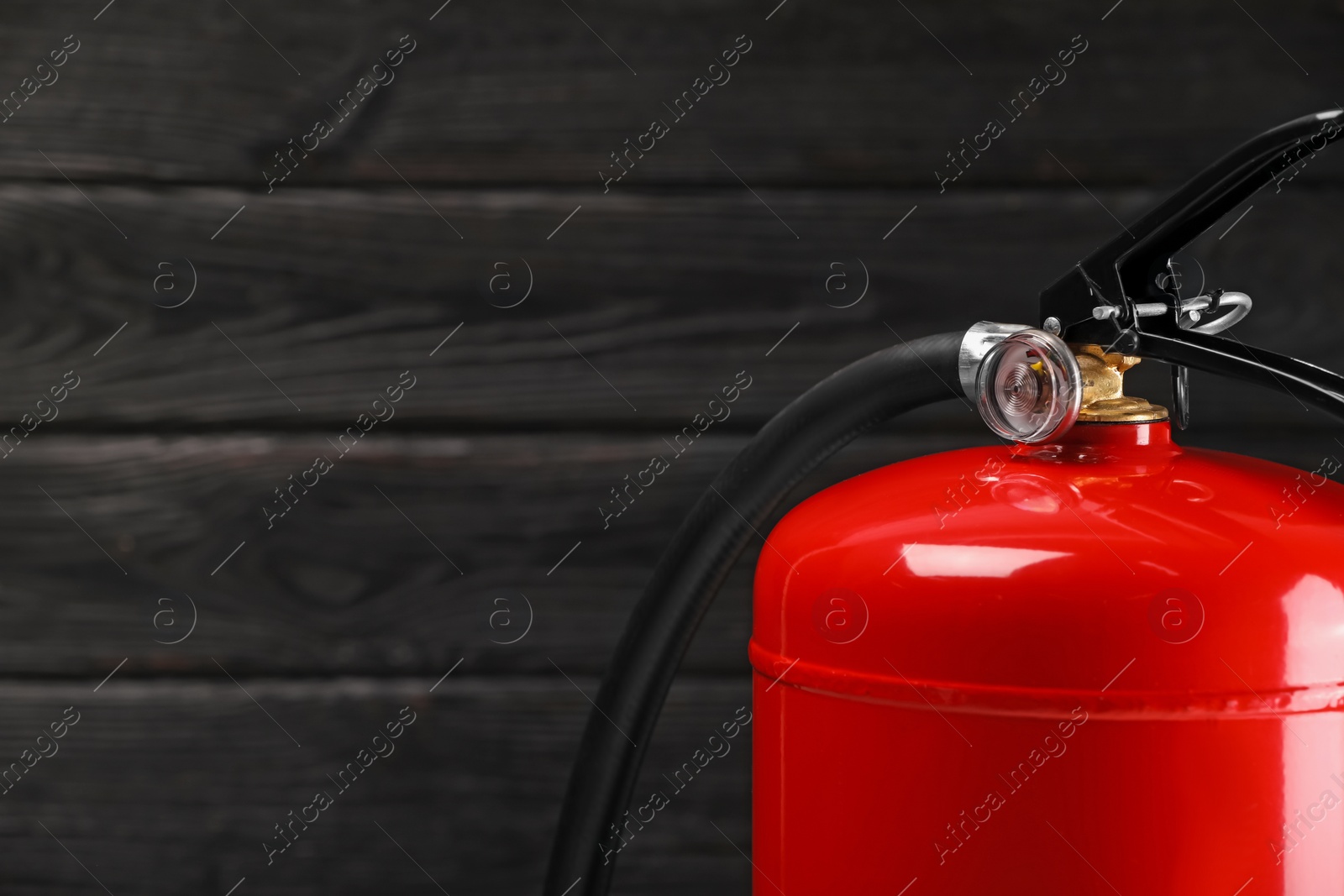 Photo of Fire extinguisher against wooden wall, closeup. Space for text