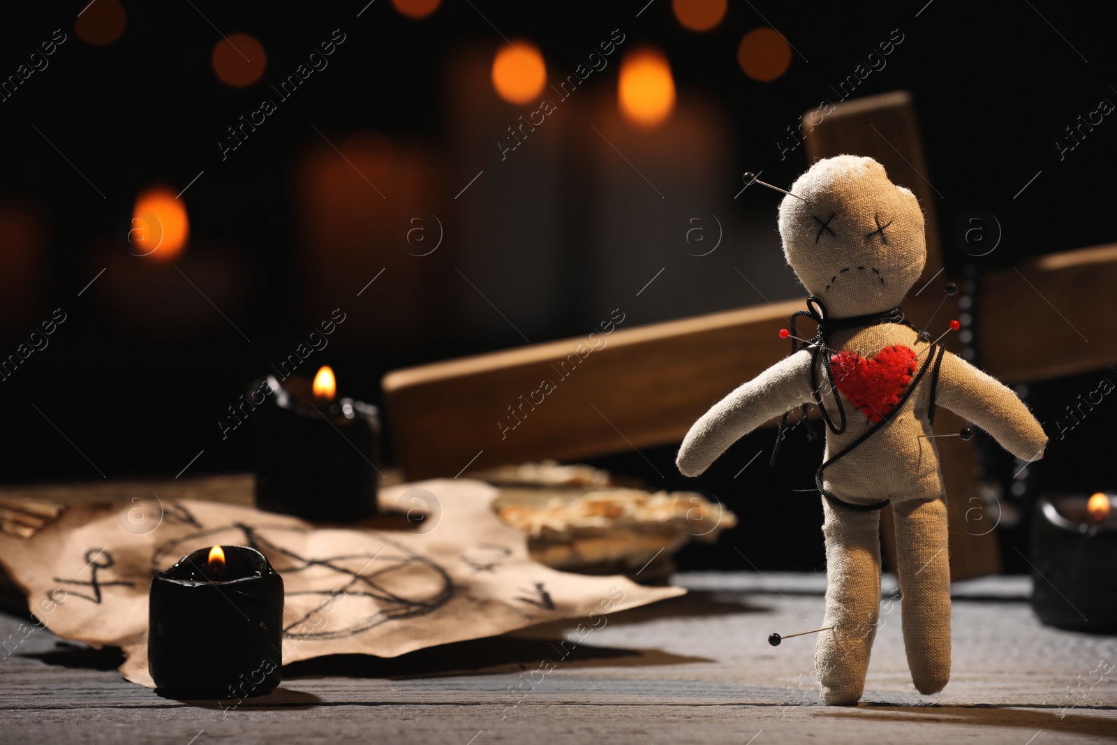 Photo of Voodoo doll pierced with pins and ceremonial items on wooden table against blurred background