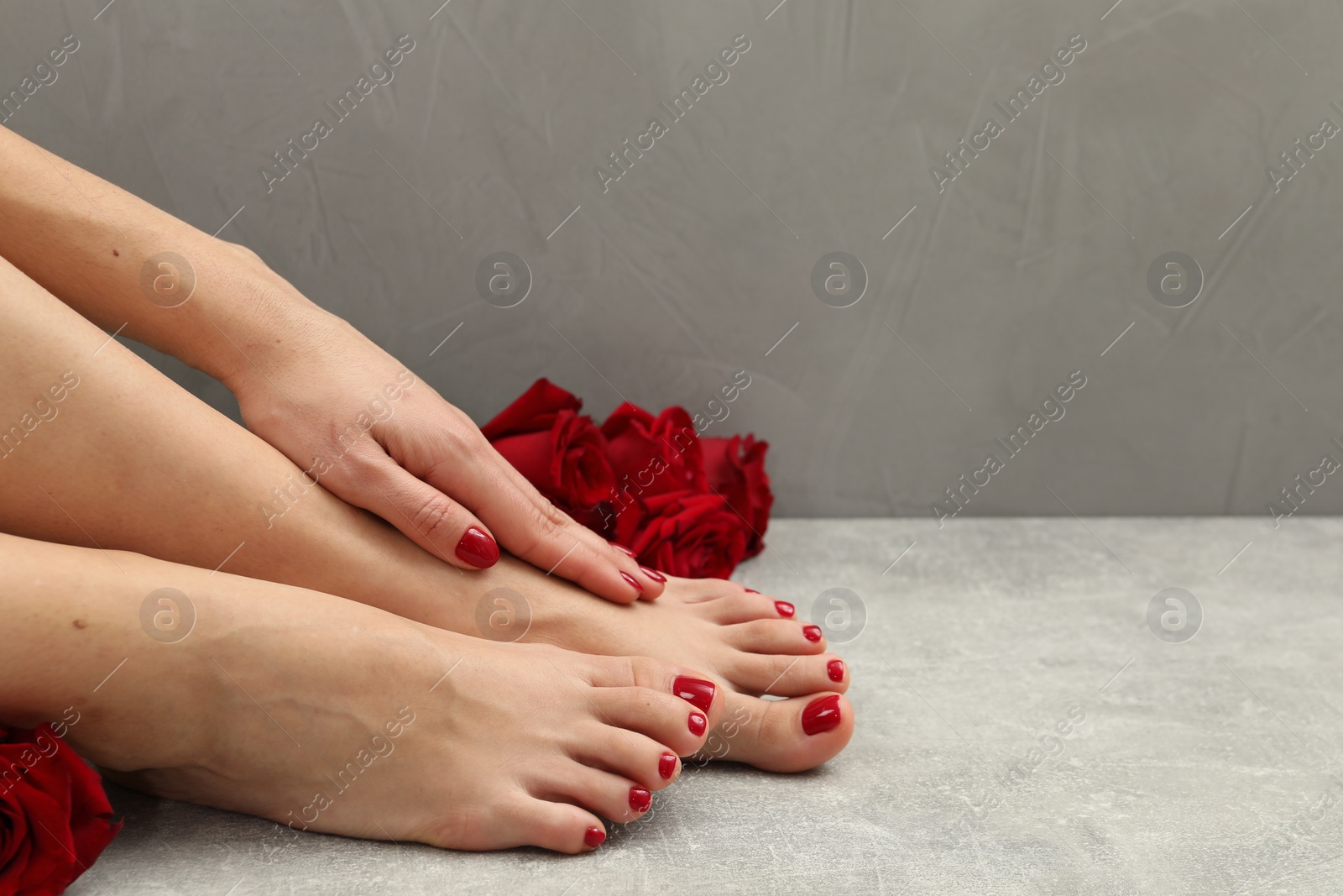 Photo of Woman with stylish red toenails after pedicure procedure and rose flowers on grey textured floor, closeup. Space for text