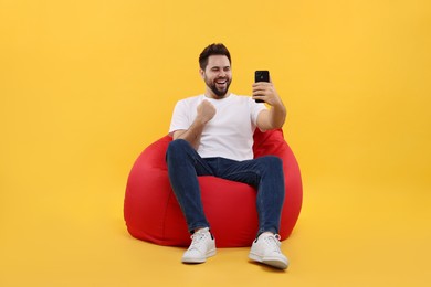 Photo of Happy young man using smartphone on bean bag chair against yellow background