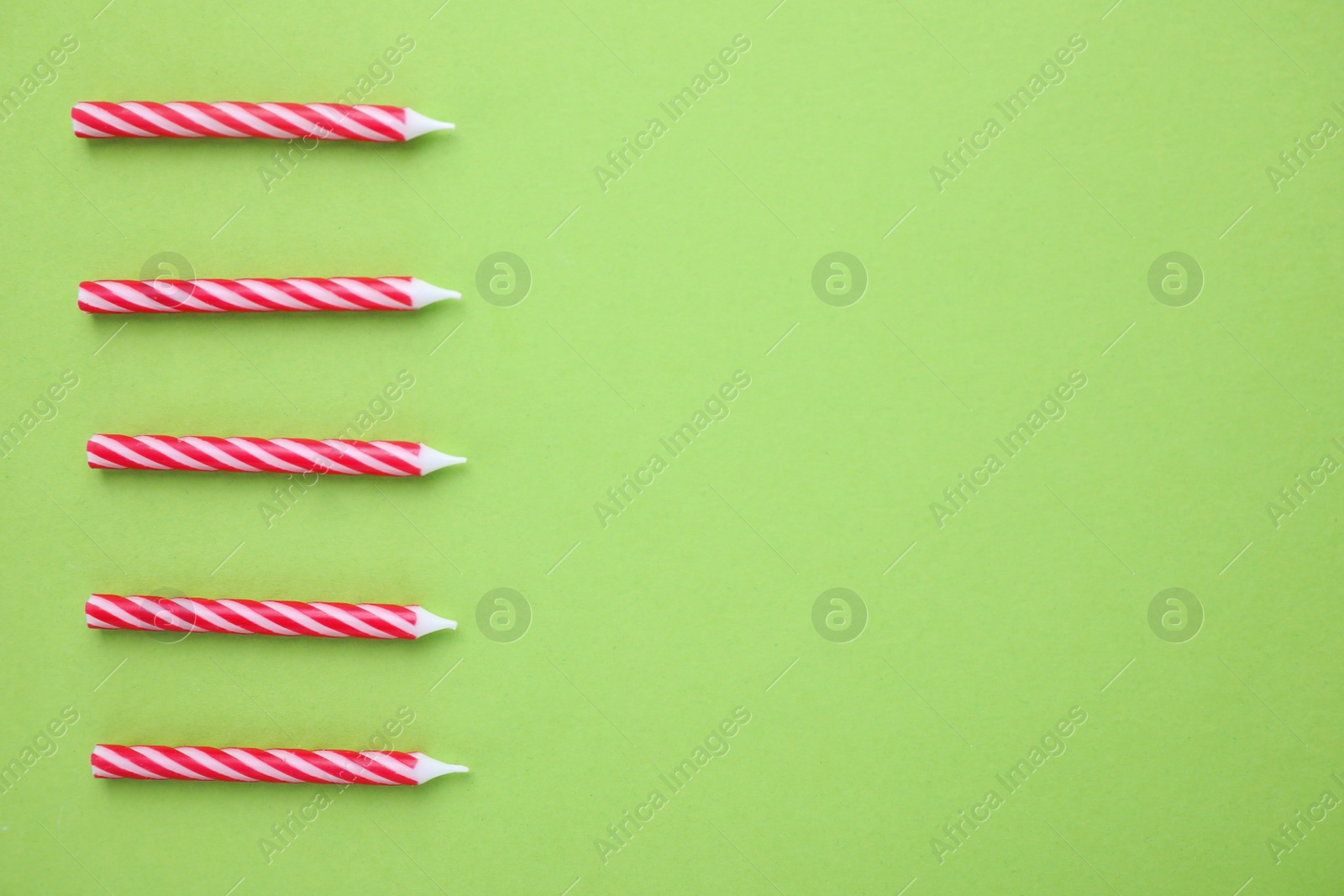 Photo of Red striped birthday candles on green background, top view with space for text