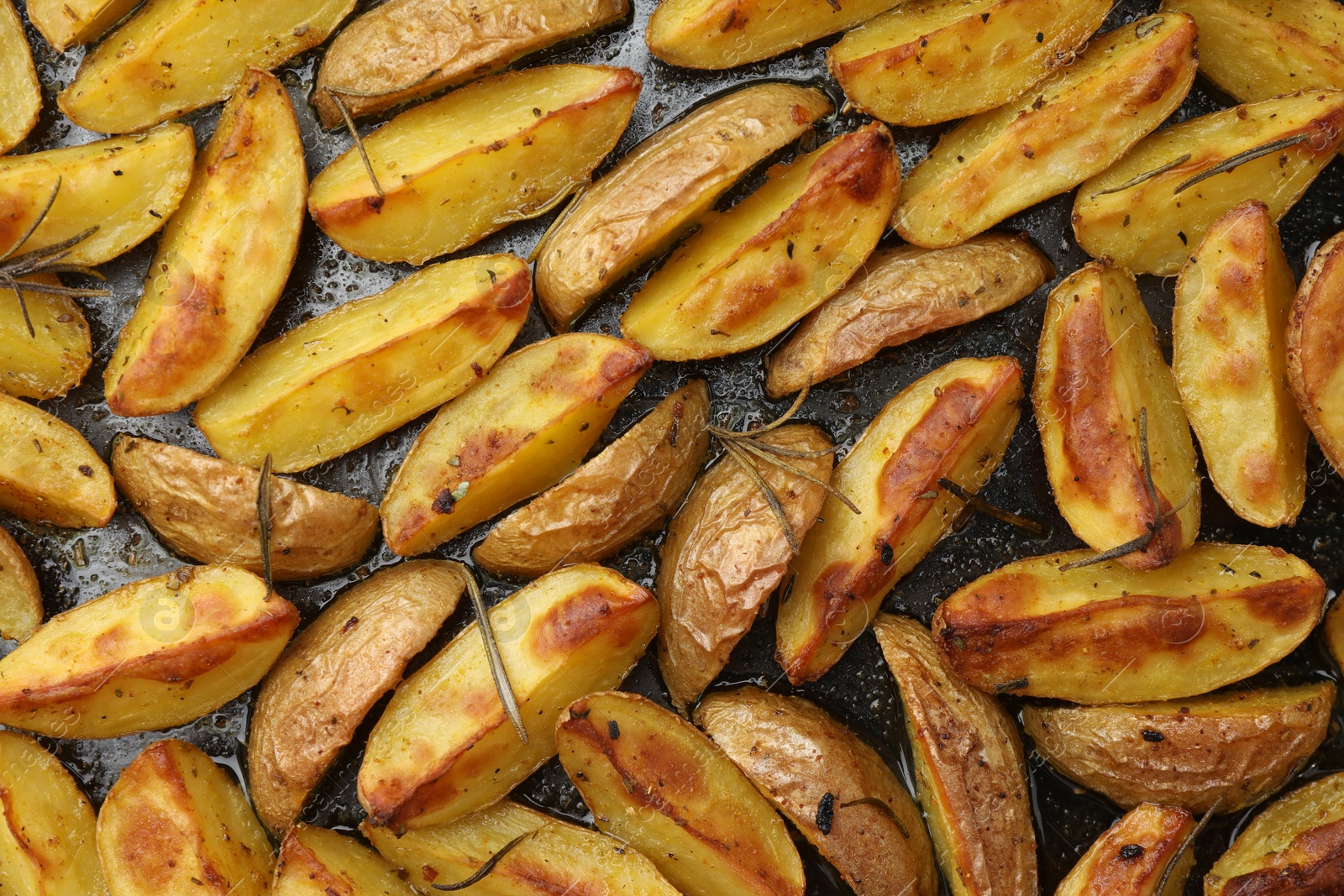 Photo of Delicious baked potatoes with rosemary on black surface, flat lay