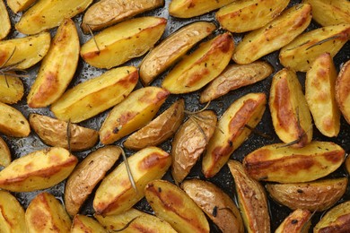 Photo of Delicious baked potatoes with rosemary on black surface, flat lay