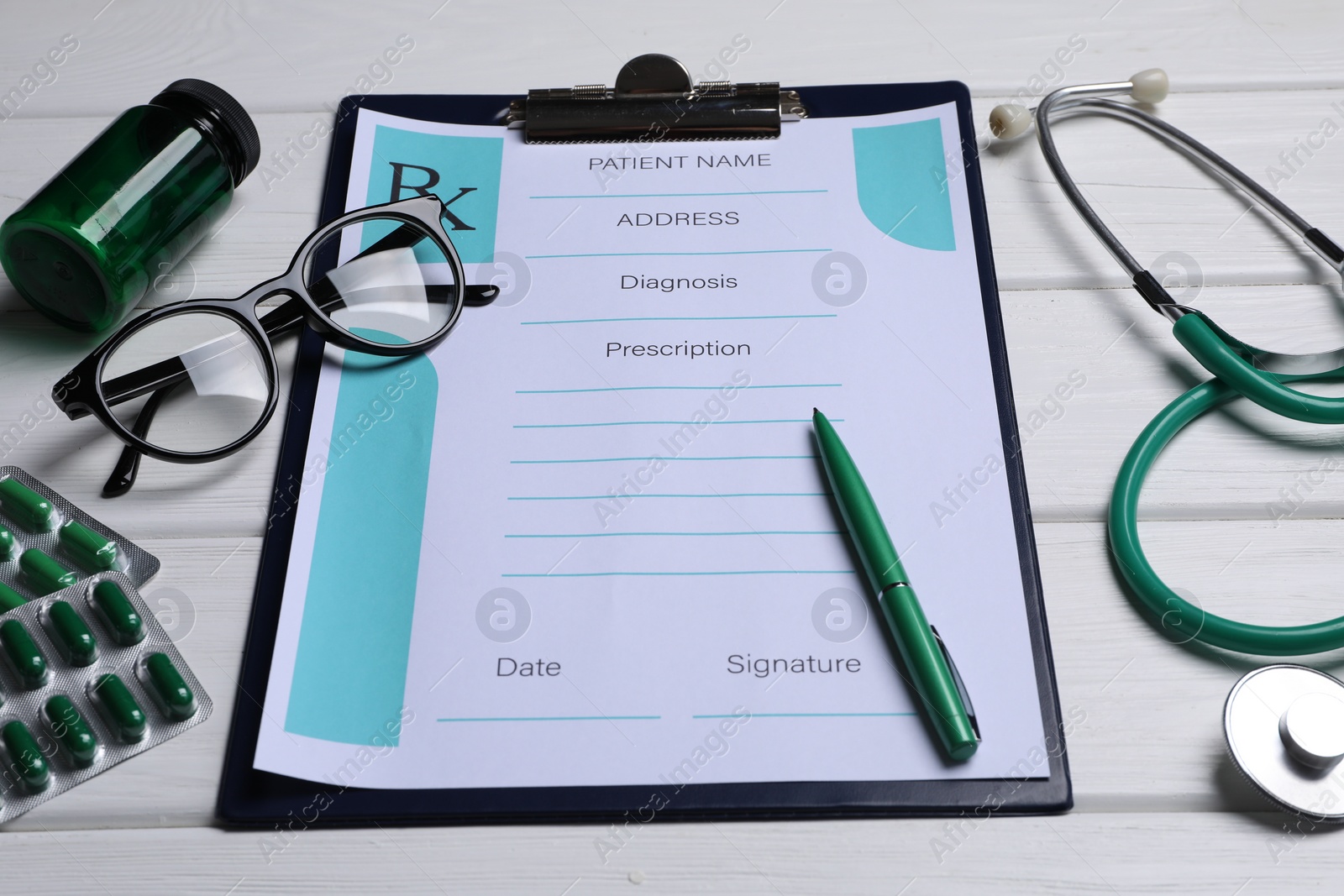 Photo of Clipboard with medical prescription form, stethoscope, pills and glasses on white wooden table