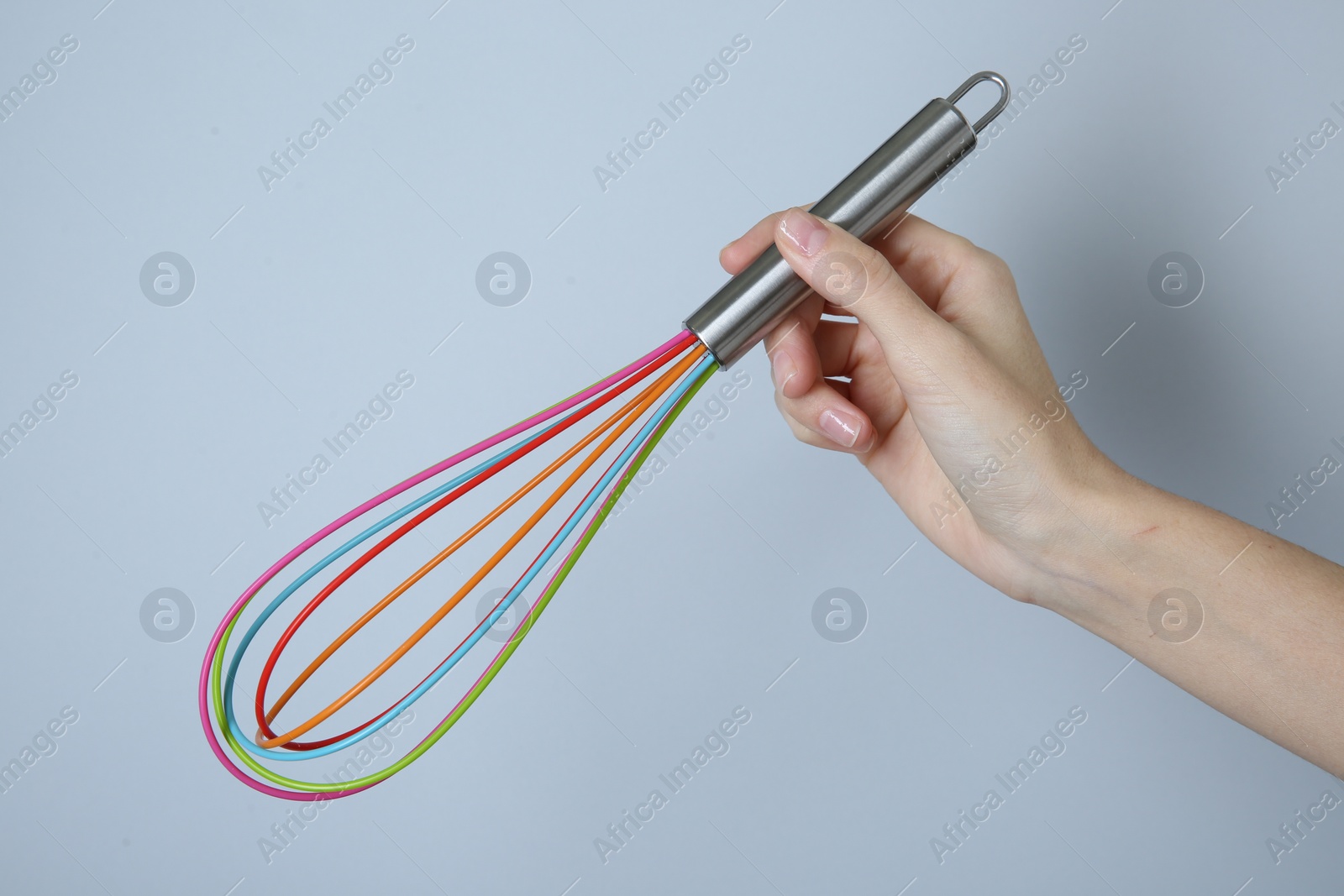 Photo of Woman holding colorful whisk on light grey background, closeup