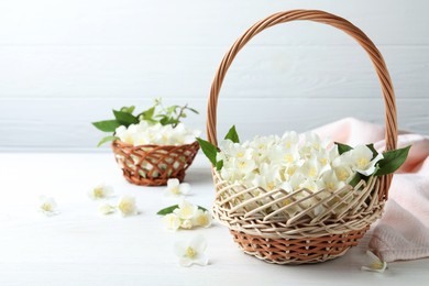 Photo of Beautiful jasmine flowers in wicker basket on white wooden table. Space for text