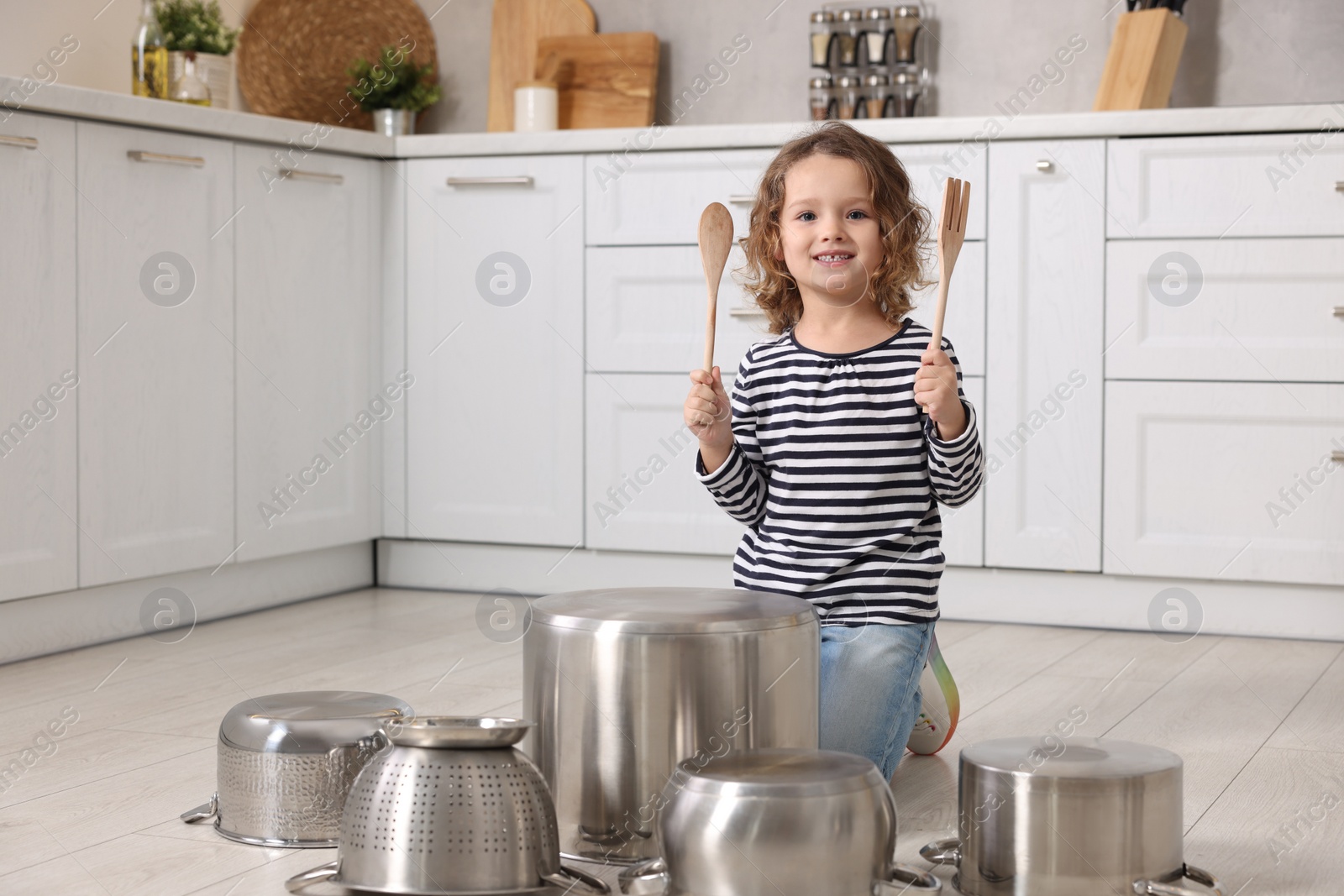 Photo of Little girl pretending to play drums on pots in kitchen